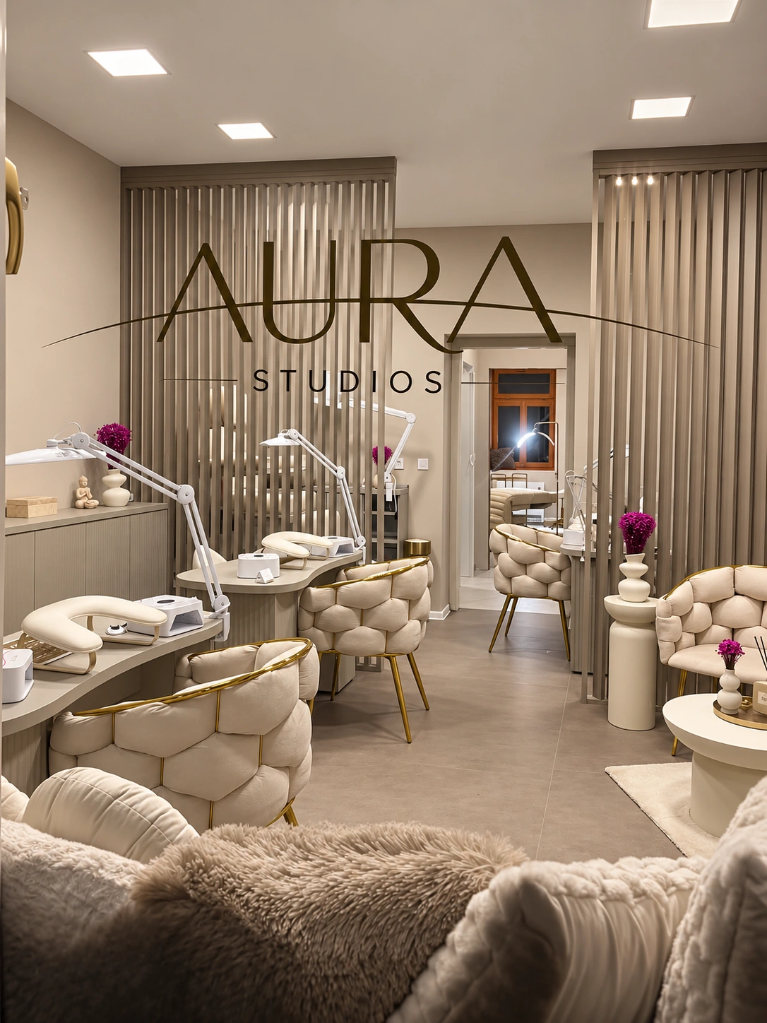 Salon Aura Studios: tři manikérské stolky, prošívaná křesla se zlatými rámy a zlatý nápis AURA STUDIOS na stěně